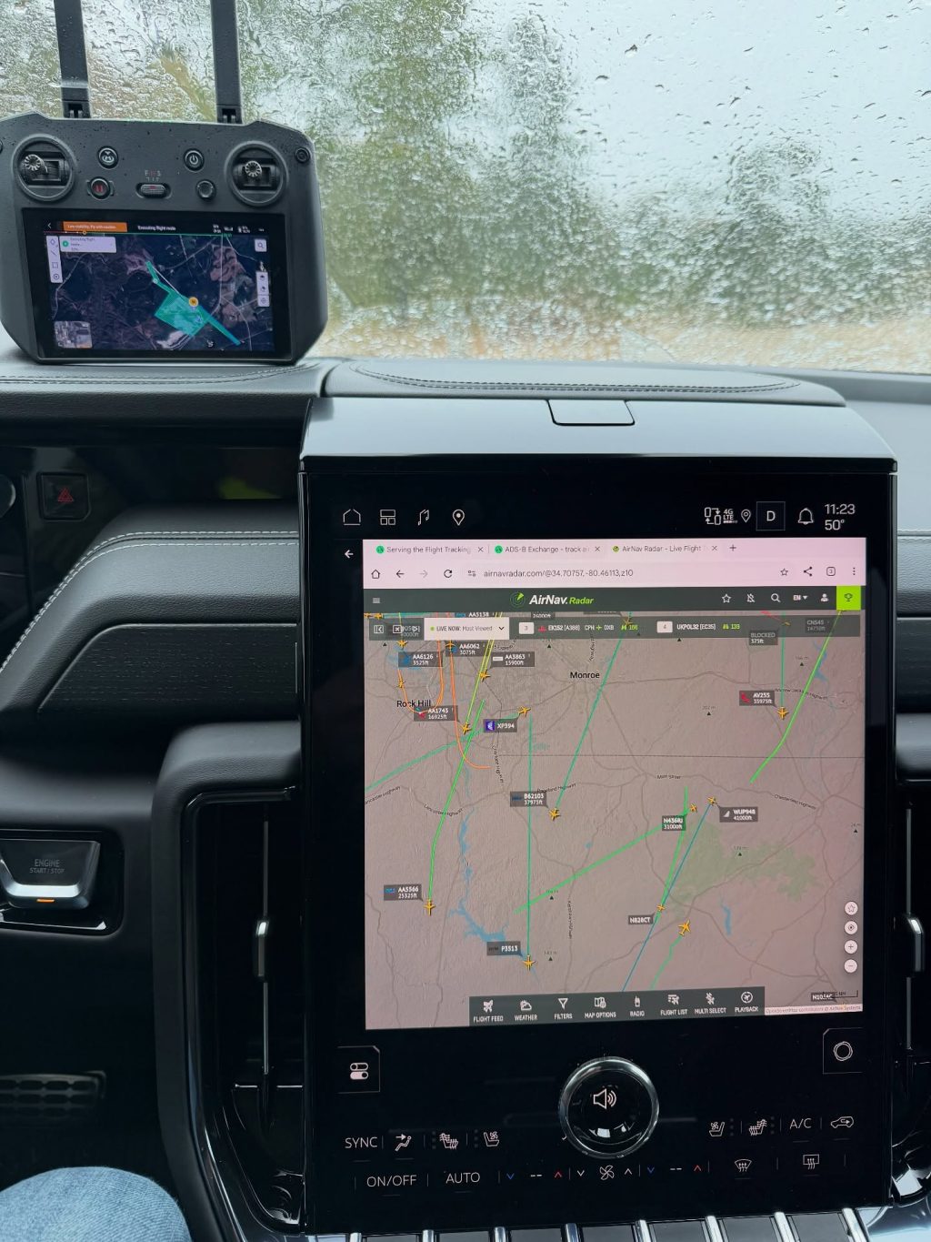 Drone controller screen and truck dashboard AirNav aircraft map seen through a rain-streaked windshield during a rainy UAV mapping job