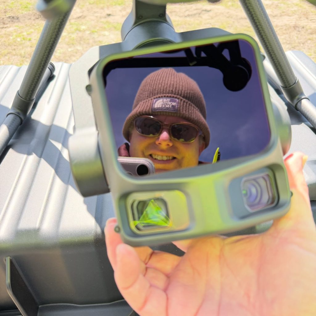 Close-up of a DJI drone with L3 LiDAR sensor held up to the camera, a crew member reflected in the gimbal